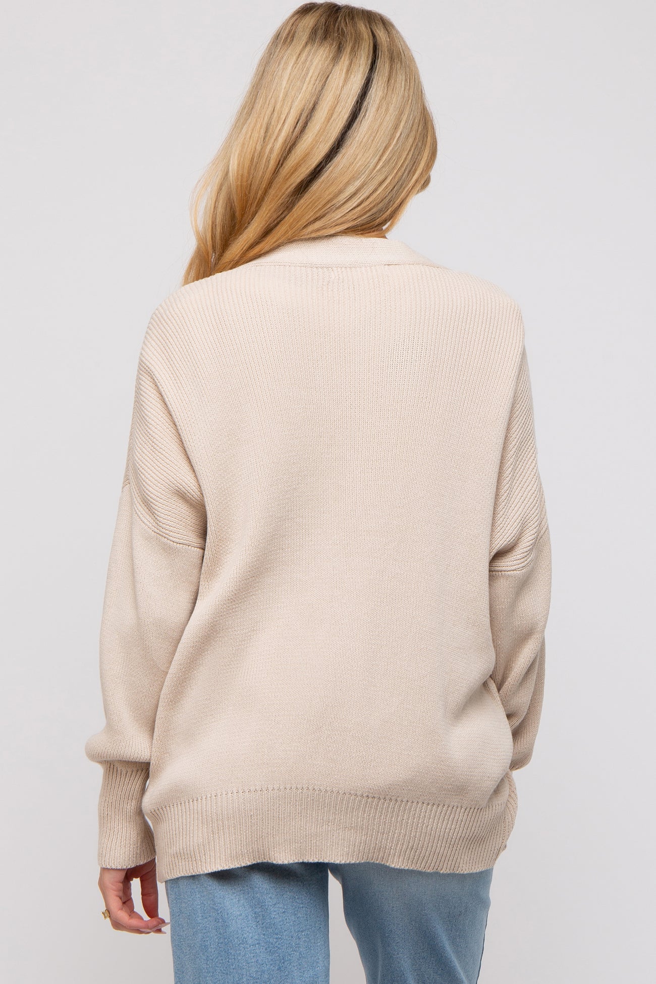 woman wearing a beige oversized maternity sweater, shown from the back, with a relaxed fit and ribbed details