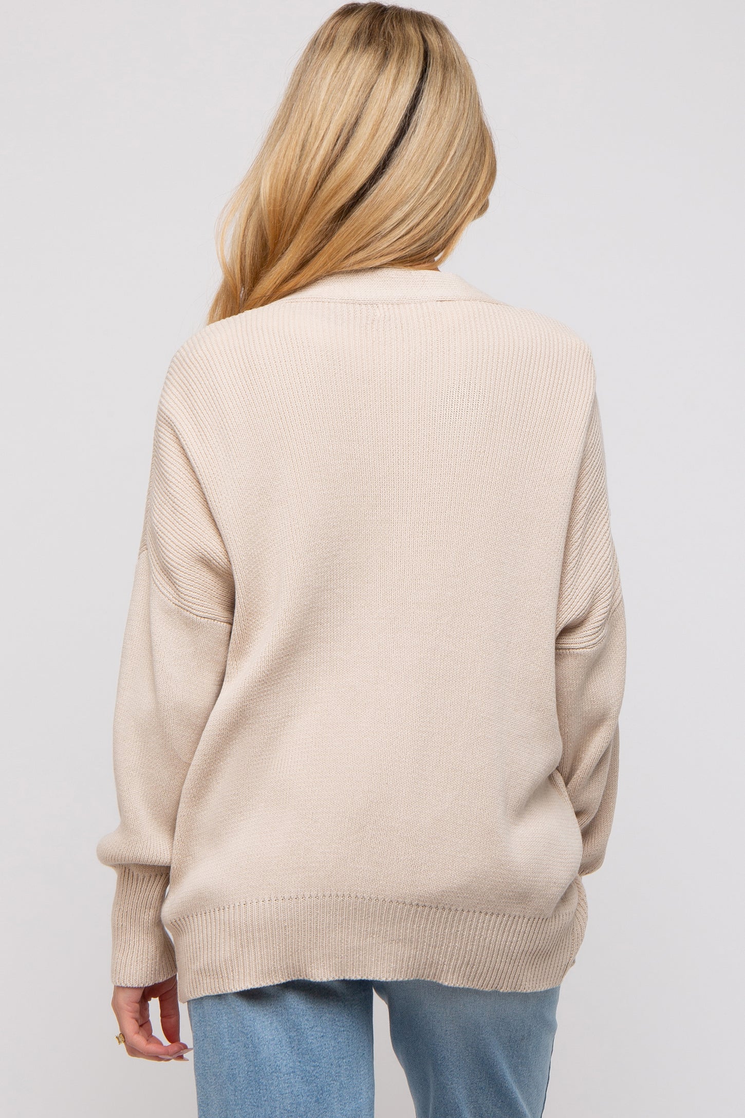woman wearing a beige oversized maternity sweater, shown from the back, with a relaxed fit and ribbed details