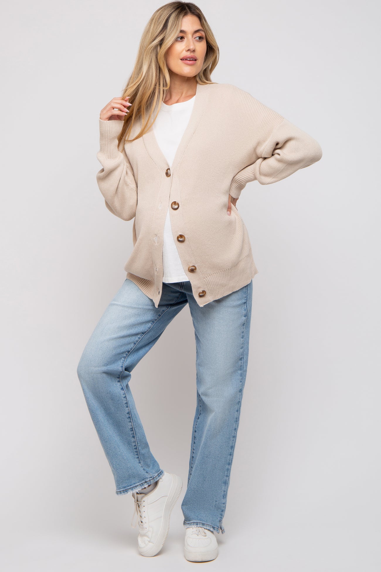 woman wearing a beige maternity cardigan over a white t-shirt and blue jeans, showing a baby bump