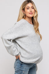 woman wearing a light gray oversized maternity sweatshirt and showing her baby bump while posing side profile