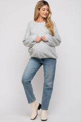 woman wearing a gray maternity sweater and blue jeans, gently cradling her baby bump with a relaxed pose