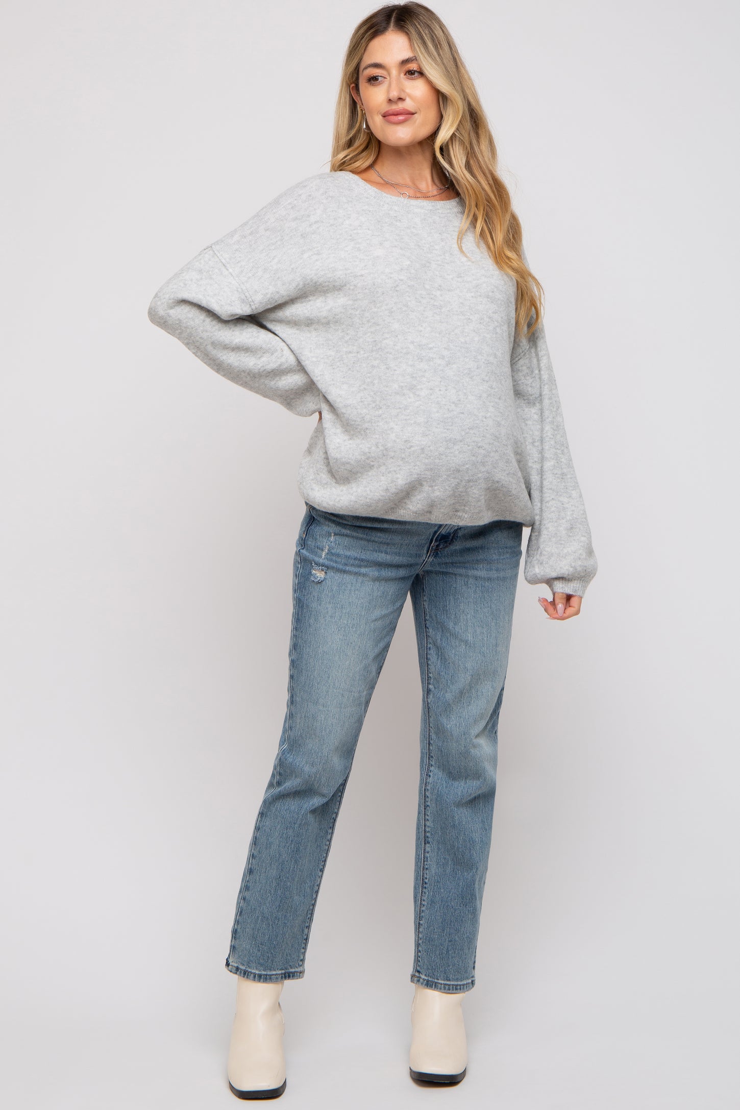 woman wearing a gray oversized maternity sweater and light wash jeans, with a visible baby bump