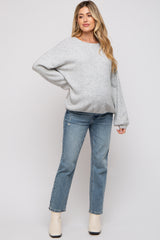 woman wearing a gray oversized maternity sweater and light wash jeans, with a visible baby bump