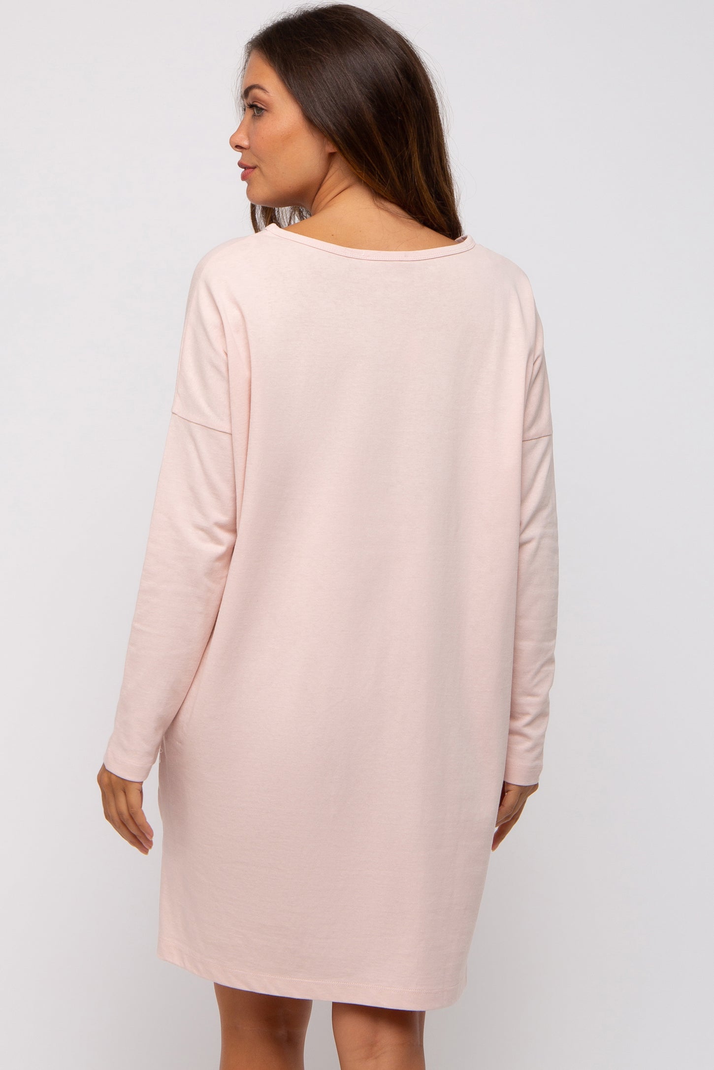 woman wearing a soft pink maternity dress with long sleeves, showing a relaxed fit and back view