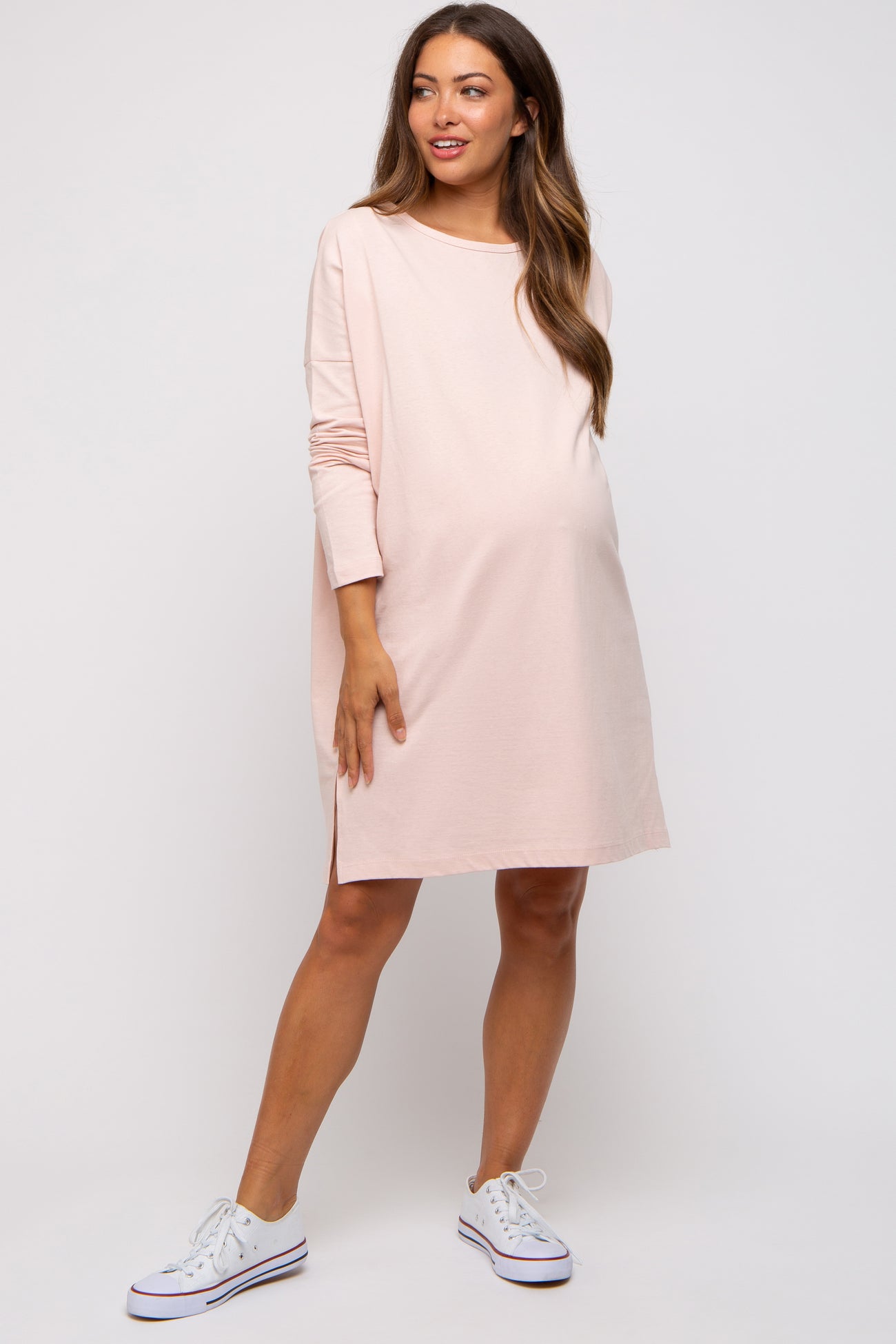 woman wearing a light pink long sleeve maternity dress with a side slit and a visible baby bump