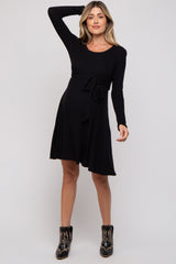 woman wearing a black long sleeve maternity dress with a tie waist and flared skirt, showing her baby bump