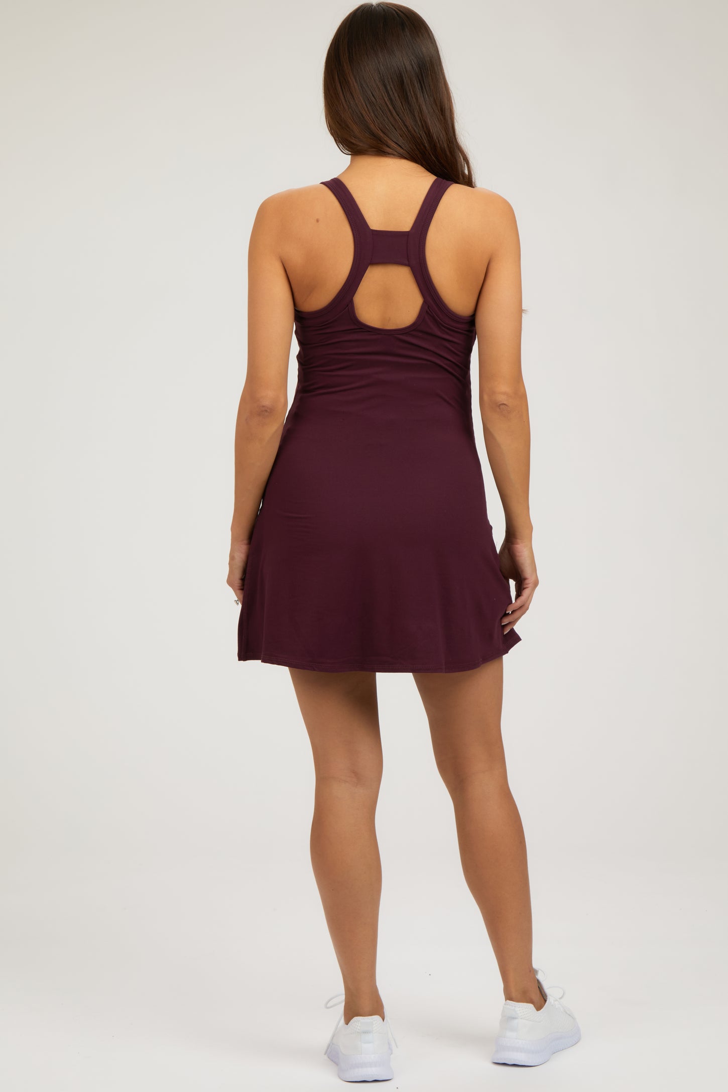 woman wearing a burgundy maternity active dress with a racerback and a flared skirt, showing her back