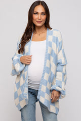 woman wearing a light blue and white checkered maternity cardigan over a white top and showing her baby bump