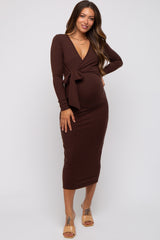 woman wearing a brown long sleeve maternity dress with a deep v-neck and tie detail, showing her baby bump