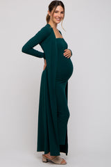 woman wearing a dark green maternity maxi dress with a matching open cardigan and showing her baby bump