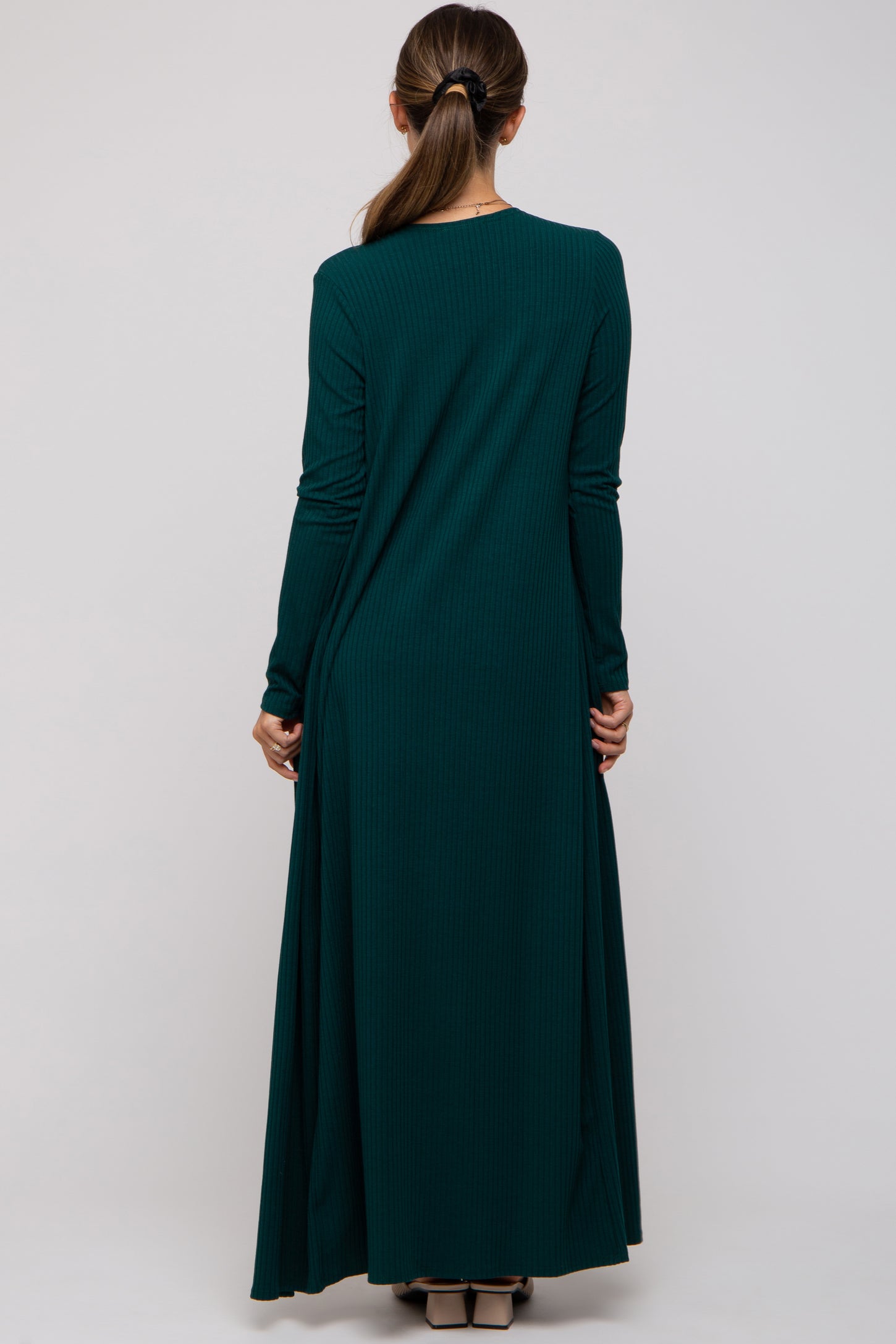 woman wearing a dark green long sleeve maternity dress, seen from the back with a flowy silhouette