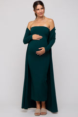 woman wearing a dark green off-the-shoulder maternity dress with a long cardigan and holding her baby bump