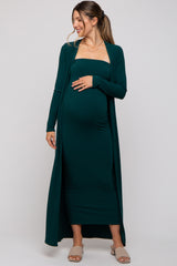 woman wearing a dark green maternity dress with a long cardigan, showing baby bump and styled with sandals