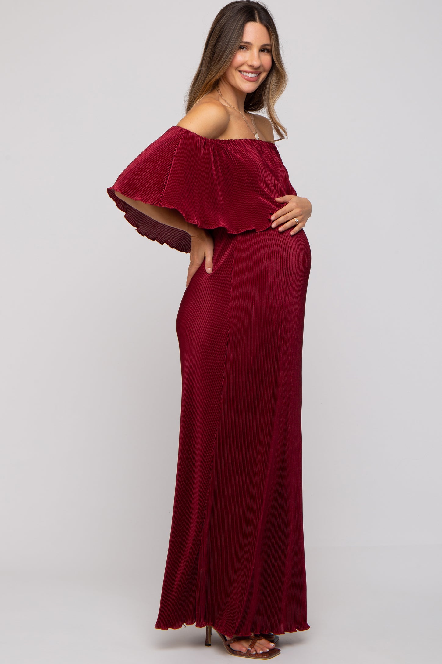 woman wearing a burgundy off-shoulder maternity maxi dress, gently holding her baby bump
