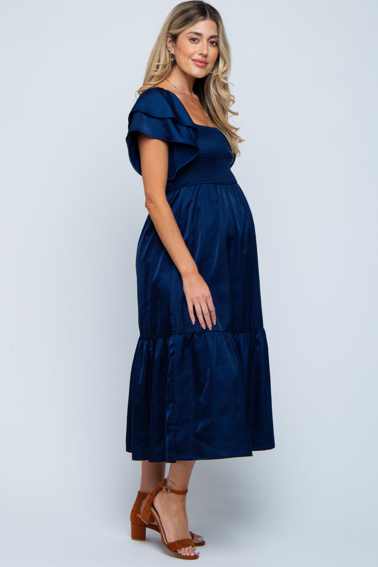 woman wearing a navy blue maternity dress with ruffle sleeves and a tiered skirt, showing her baby bump