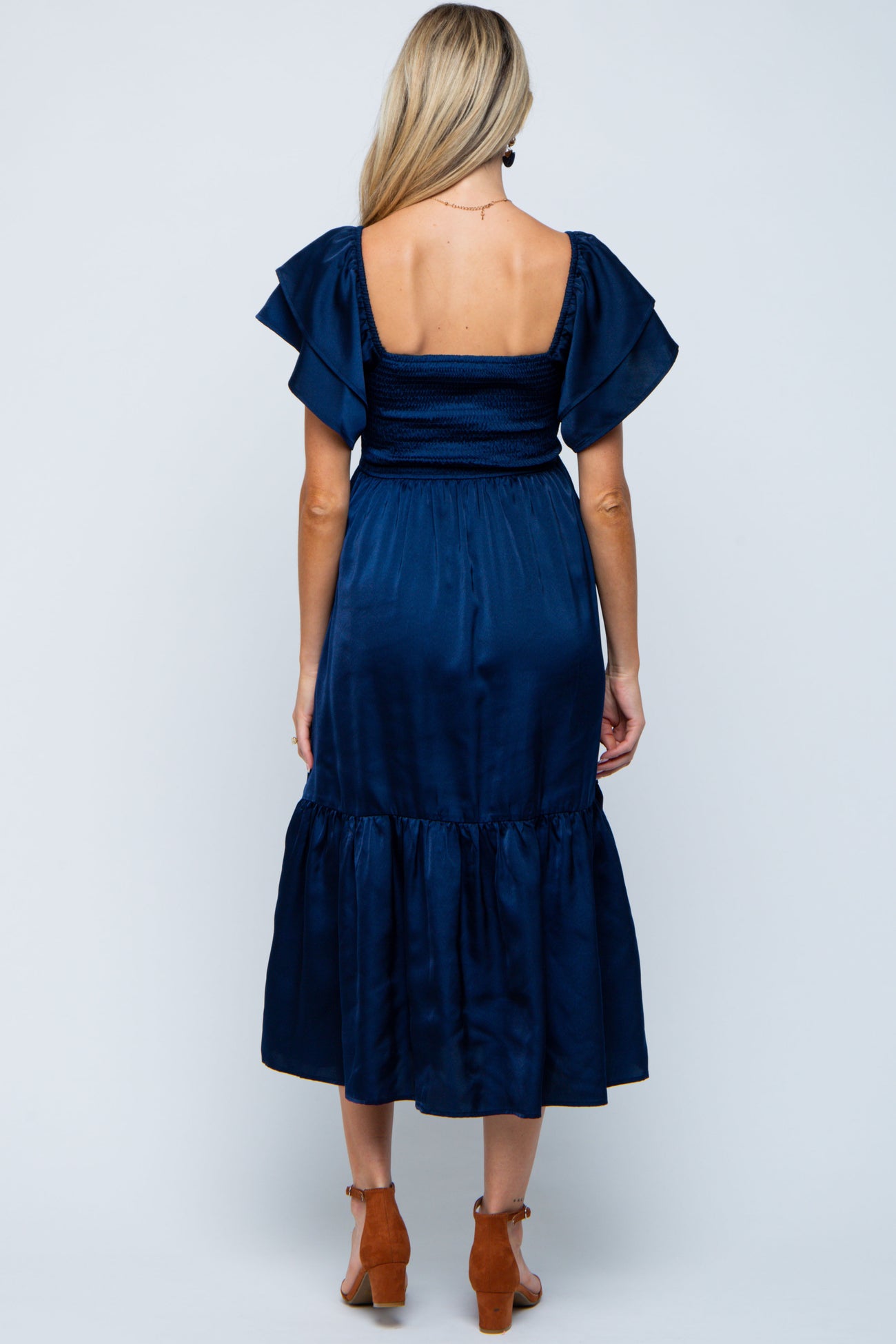 woman wearing a navy blue maternity dress with flutter sleeves and a tiered mid-length skirt, showing a baby bump