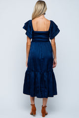 woman wearing a navy blue maternity dress with flutter sleeves and a tiered mid-length skirt, showing a baby bump