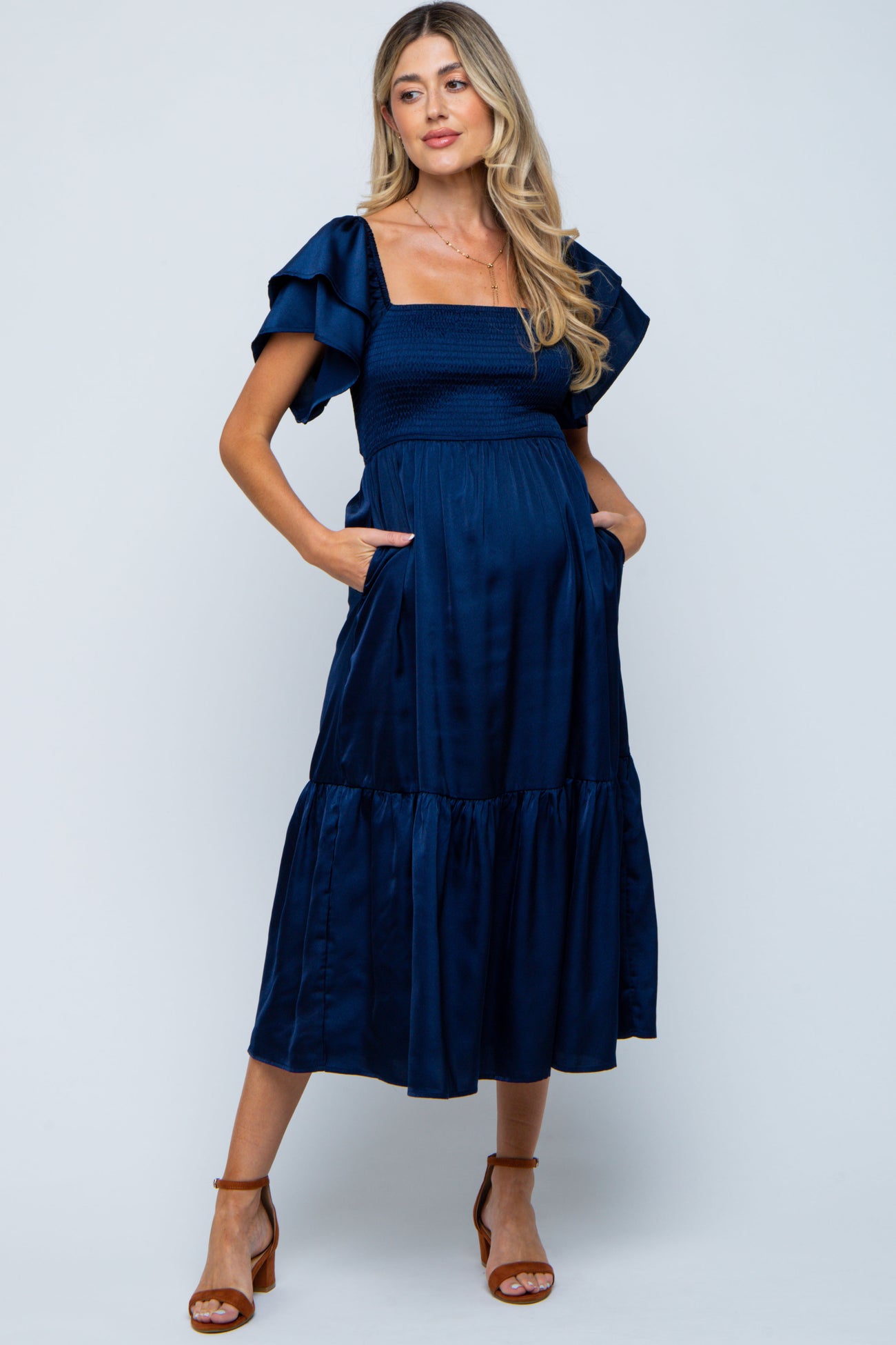 woman wearing a navy blue maternity dress with puff sleeves and pockets, featuring a tiered skirt and a visible baby bump