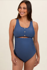 woman wearing a navy blue maternity swimsuit with scalloped edges and a cut-out design, showcasing her baby bump