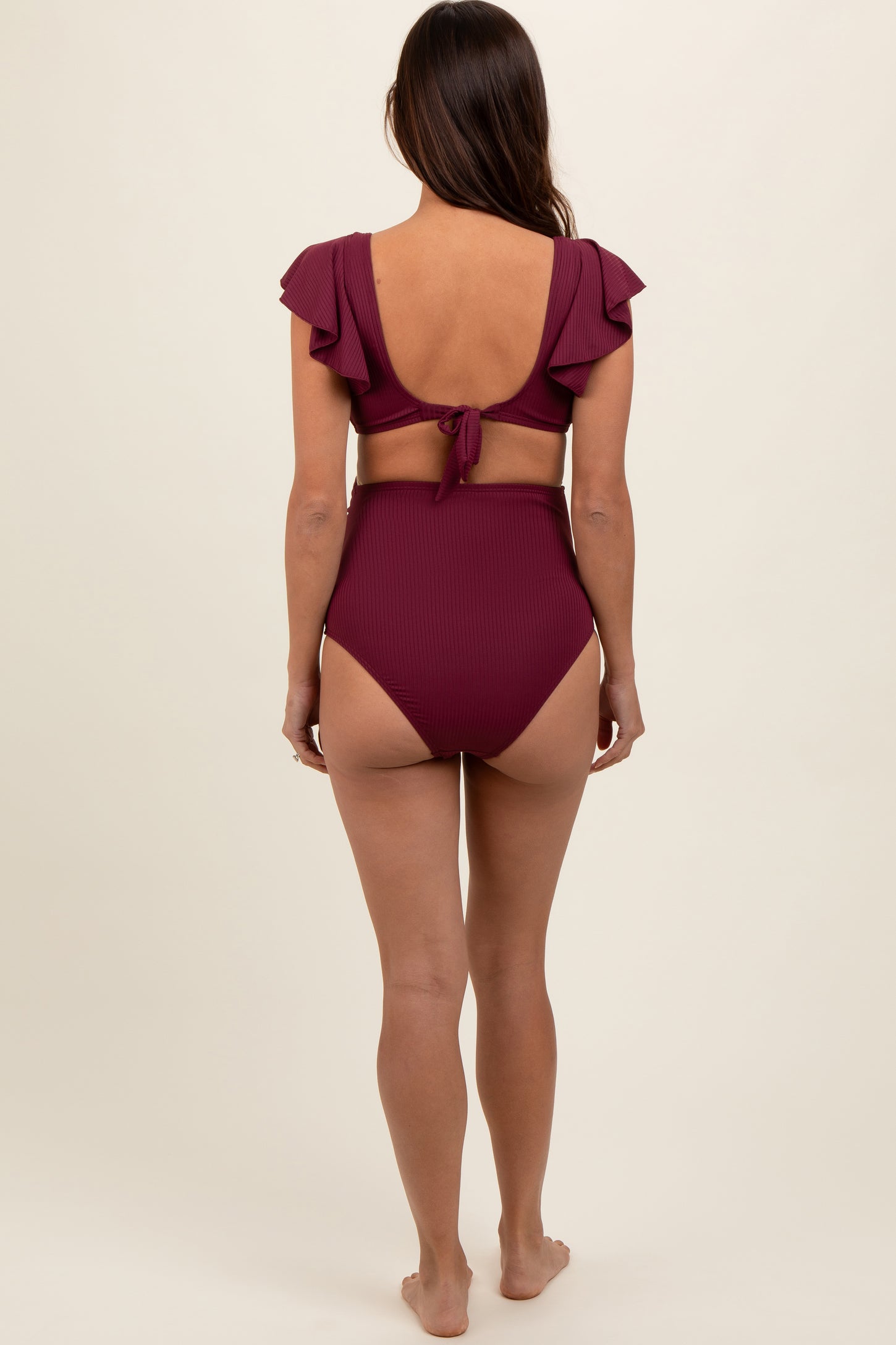 woman wearing a bordeaux maternity bikini with ruffle sleeves and high-waisted bottoms, showing a baby bump from behind