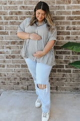 woman wearing a striped maternity blouse and light blue ripped jeans, holding her baby bump