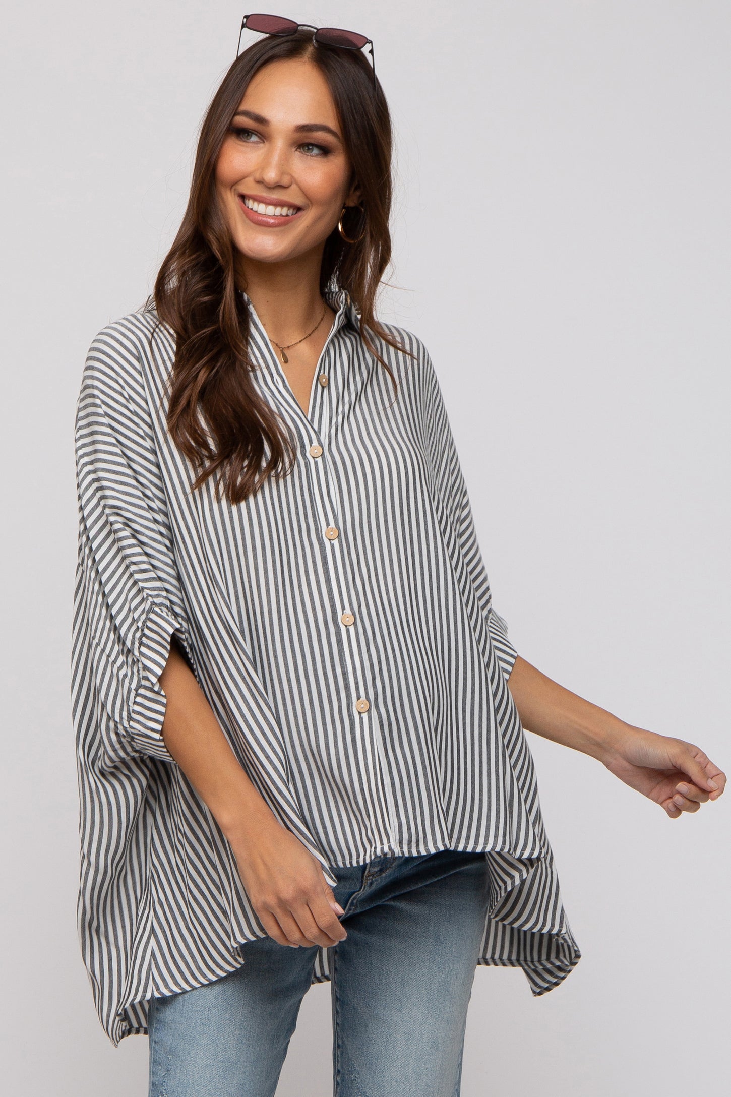 woman wearing a striped maternity top with a button-down front and relaxed fit, smiling while standing against a light background