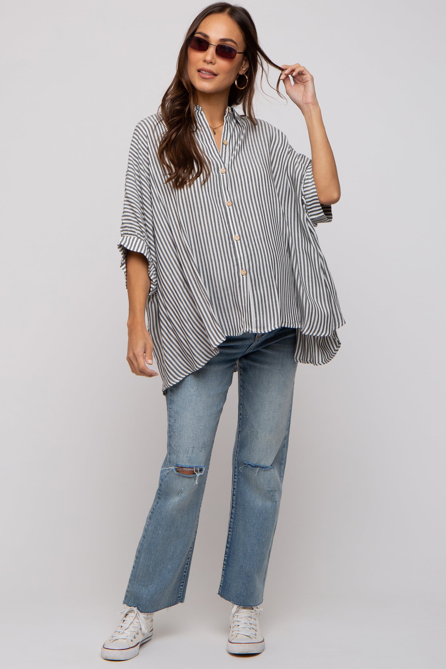 woman wearing a striped oversized maternity shirt with buttons and distressed blue jeans, styled casually with sunglasses