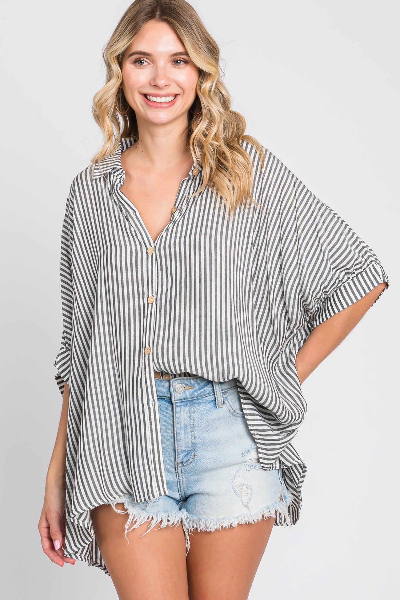 woman wearing a gray and white striped oversized button-up shirt paired with distressed denim shorts