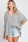 woman wearing a gray and white striped oversized button-up shirt paired with distressed denim shorts