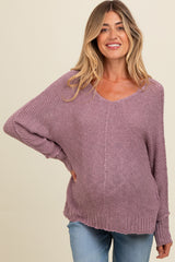woman wearing a purple oversized maternity sweater, showing her baby bump, paired with light blue jeans
