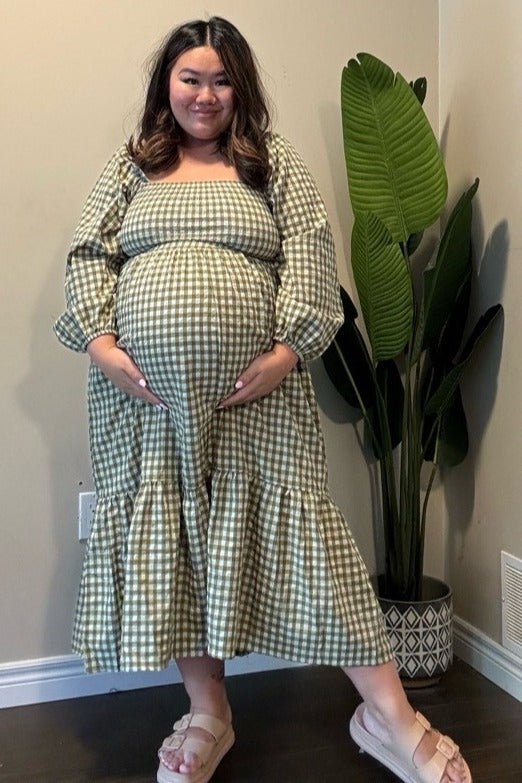 woman wearing a green and white checkered maternity dress with a ruffled hem and holding her baby bump