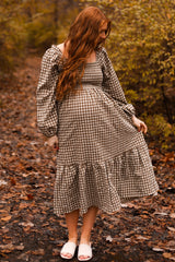 woman wearing a brown and white checkered maternity dress with long puff sleeves and a flared hem, showing her baby bump