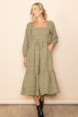 woman wearing a green and beige plaid midi dress with long sleeves and a tiered skirt, standing against a neutral background