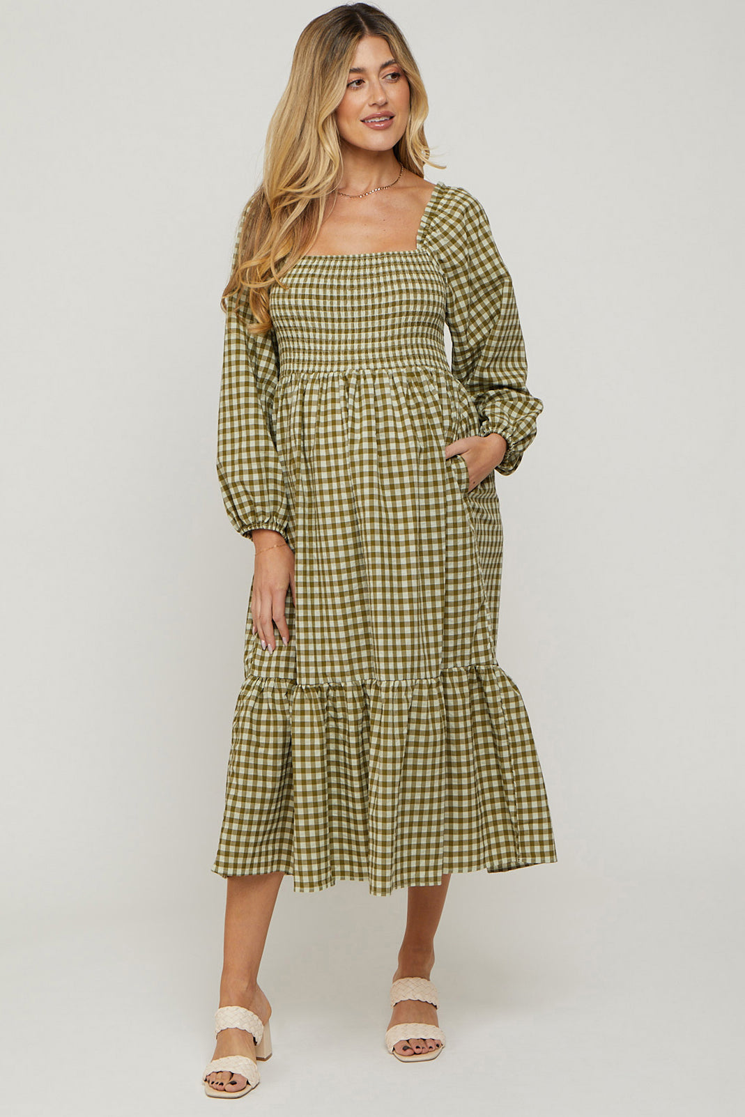 woman wearing a green and white checkered maternity dress with puff sleeves and a tiered hem, smiling at the camera