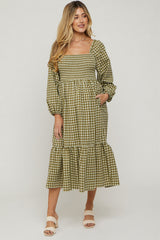 woman wearing a green and white checkered maternity dress with puff sleeves and a tiered hem, smiling at the camera