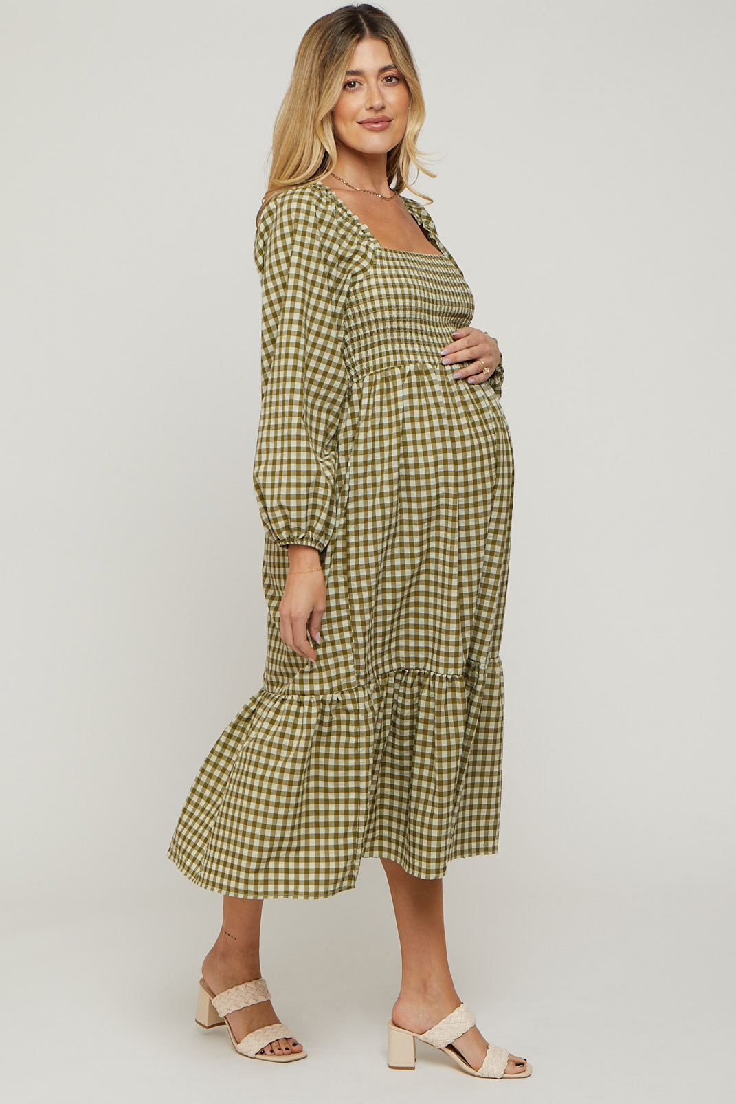 woman wearing a green and tan checked maternity dress with puff sleeves and a tiered skirt, holding her baby bump