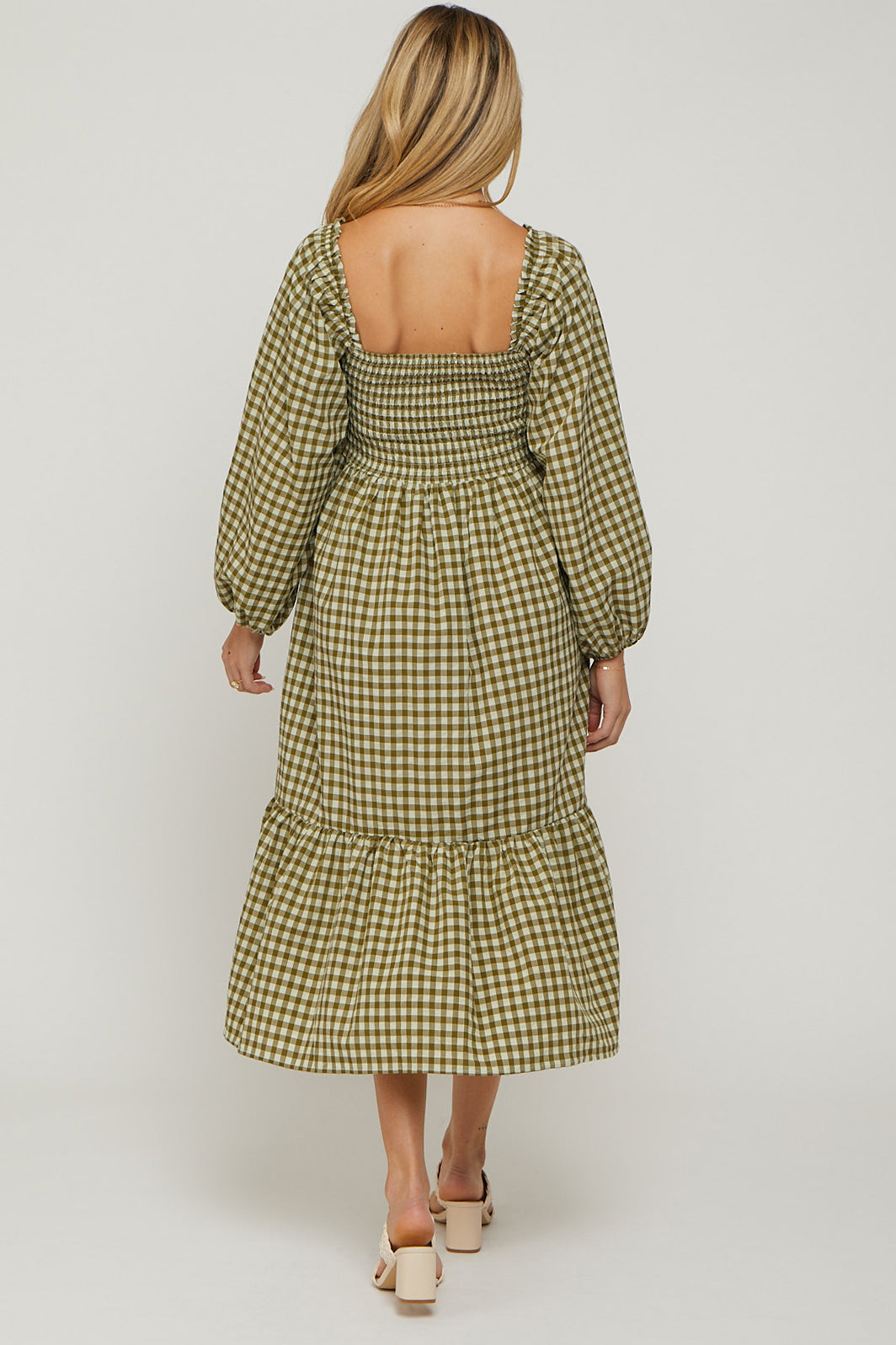 woman wearing a green and white gingham maternity dress with puffed sleeves and a tiered hem, showing a baby bump
