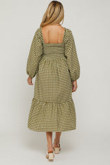 woman wearing a green and white gingham maternity dress with puffed sleeves and a tiered hem, showing a baby bump