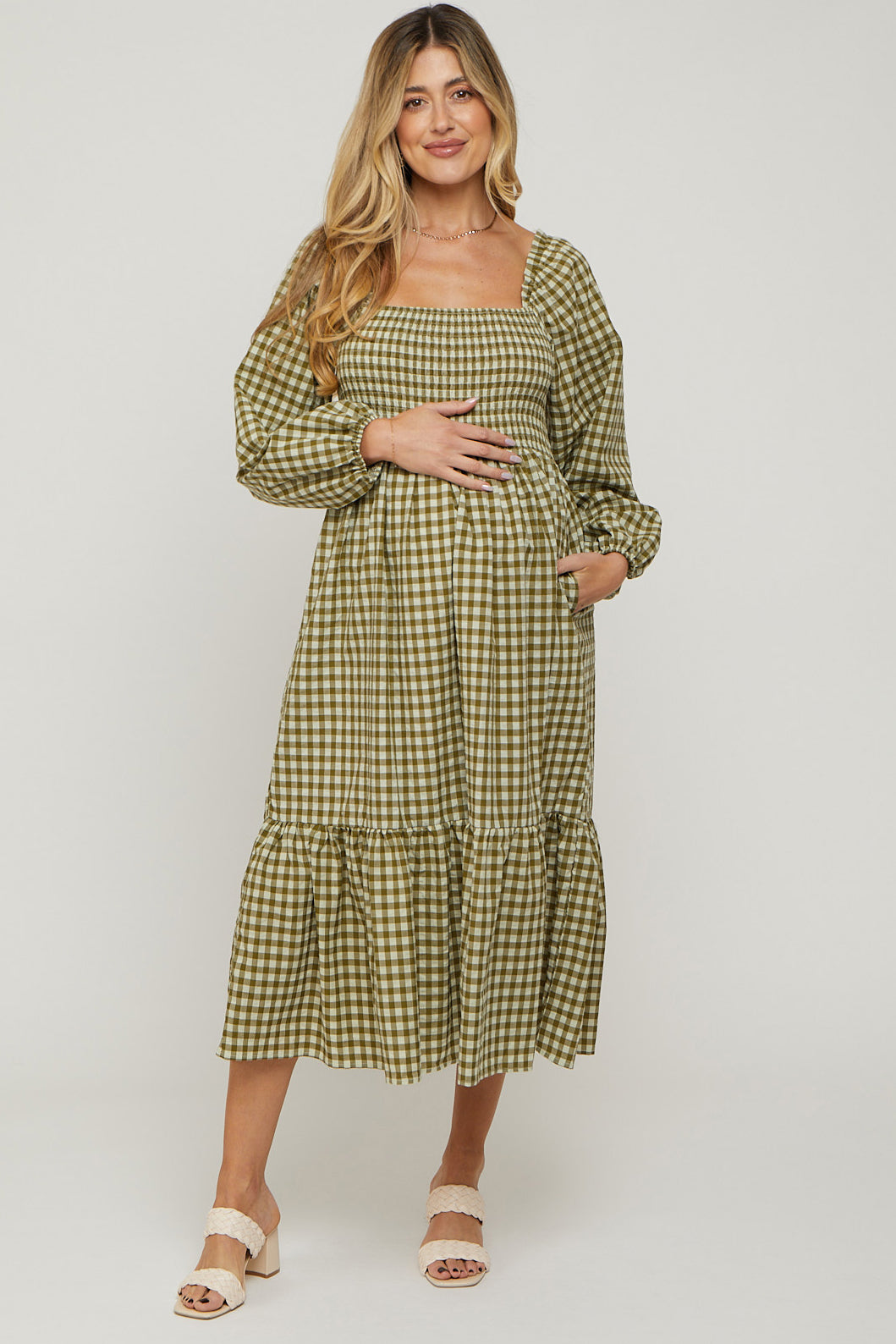 woman wearing a green and beige checkered maternity dress with long sleeves and a flared hem, holding her baby bump