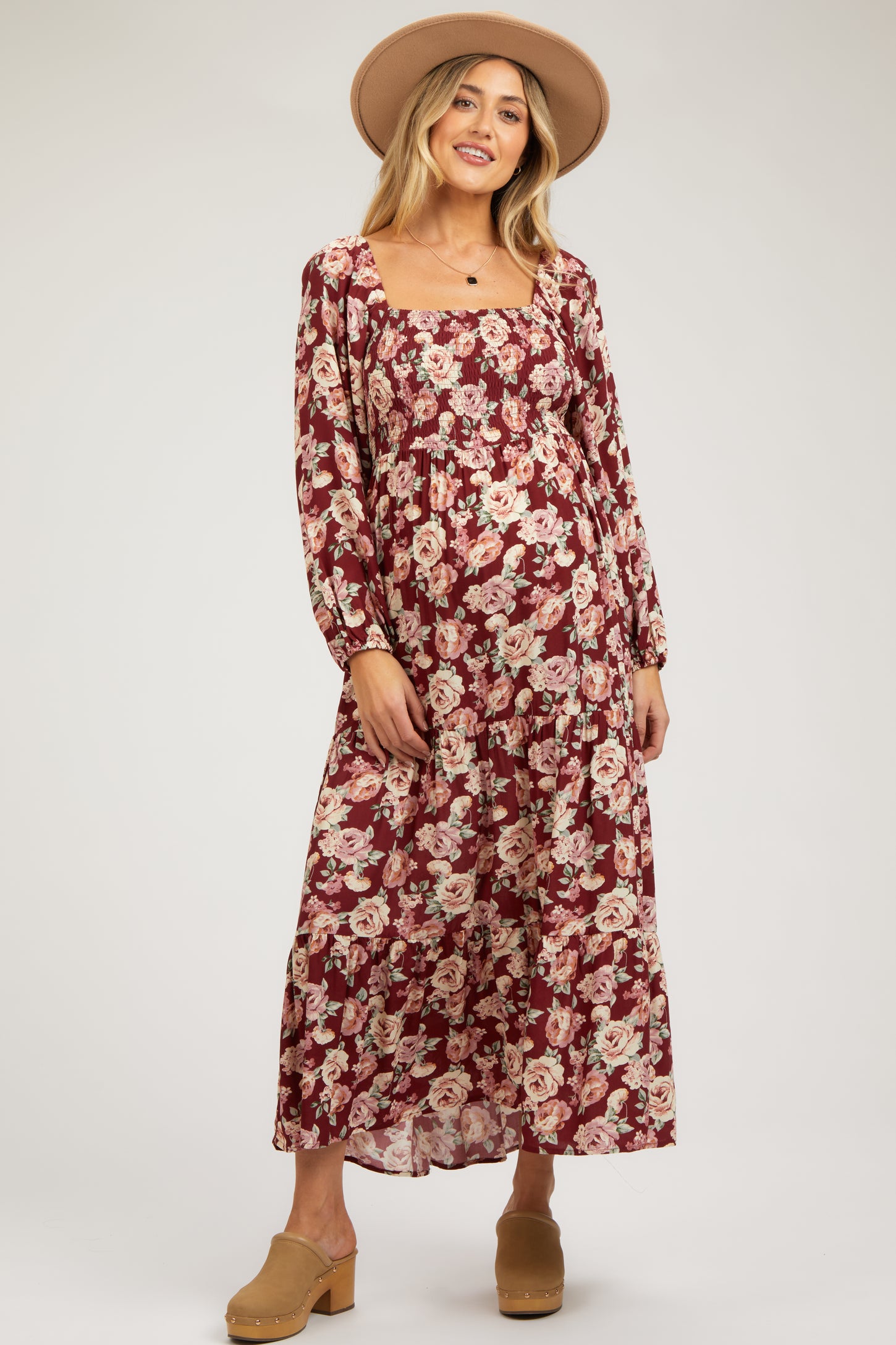 woman wearing a burgundy floral maternity dress with long sleeves and a ruffled skirt, showcasing her baby bump