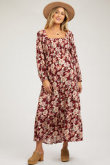 woman wearing a burgundy floral maternity dress with long sleeves and a ruffled skirt, showcasing her baby bump