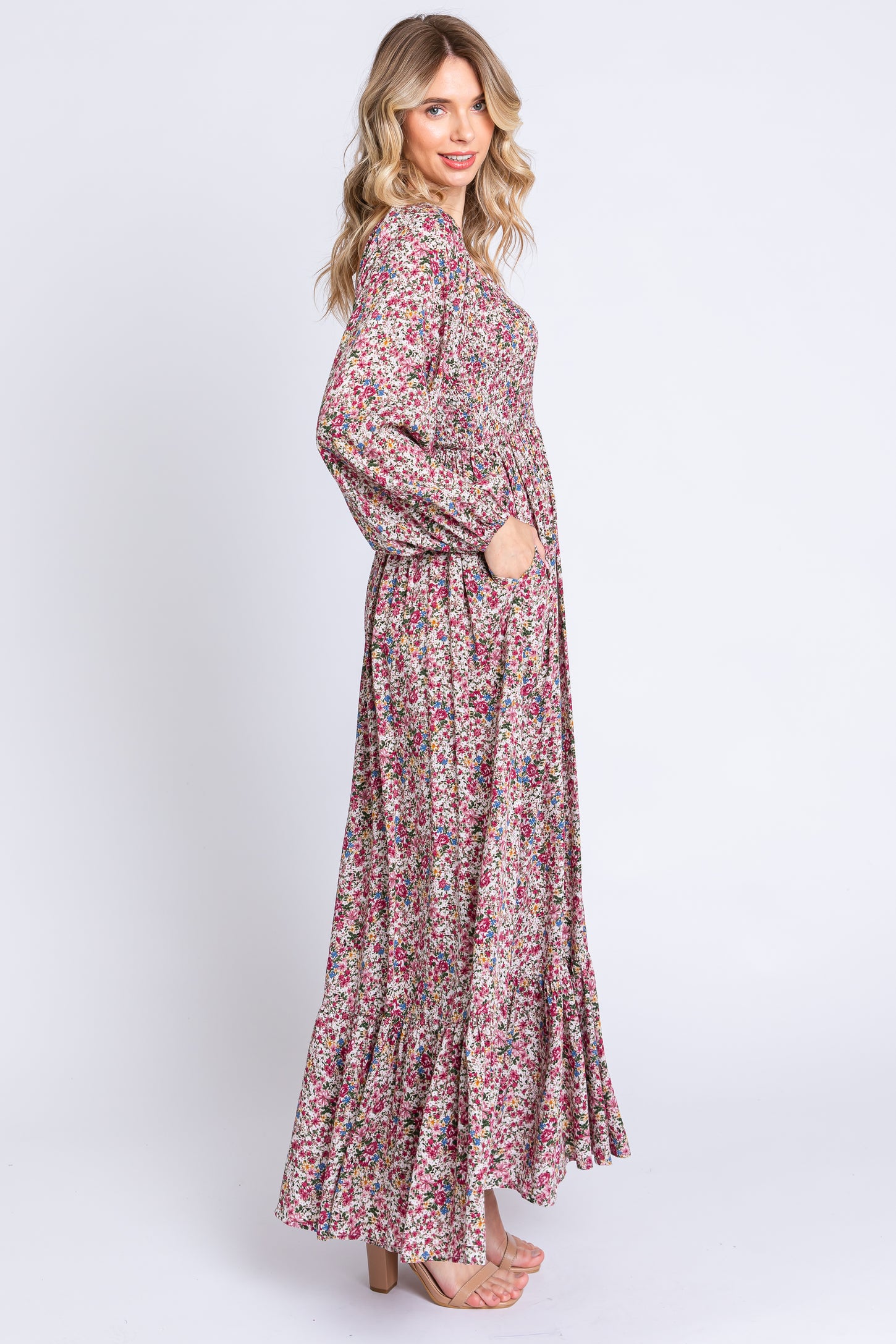 woman wearing a long floral print maxi dress with long sleeves and a ruffled hem, posing with her hands in pockets