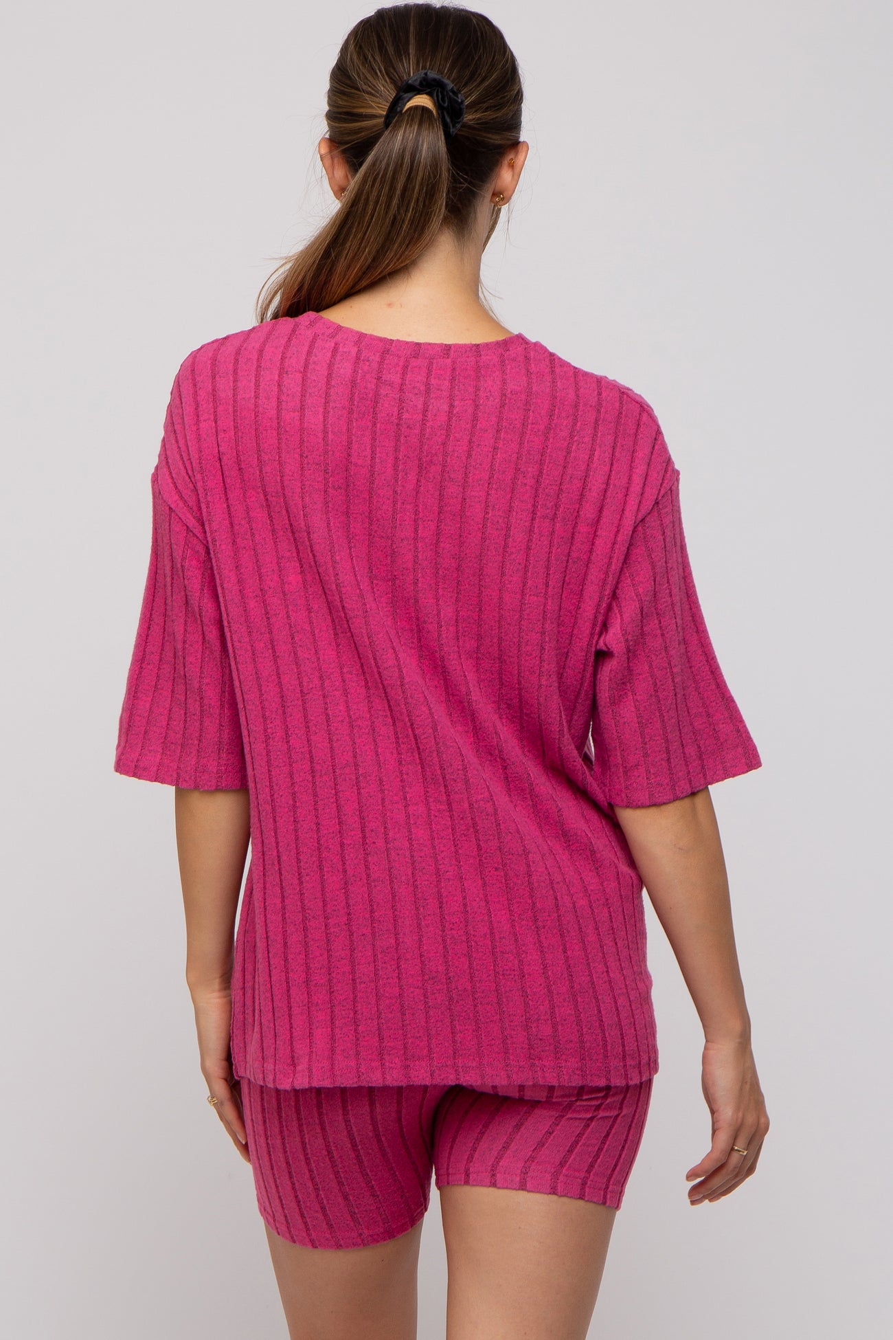woman wearing a pink ribbed maternity loungewear set with a short sleeve top and matching shorts, showing her back