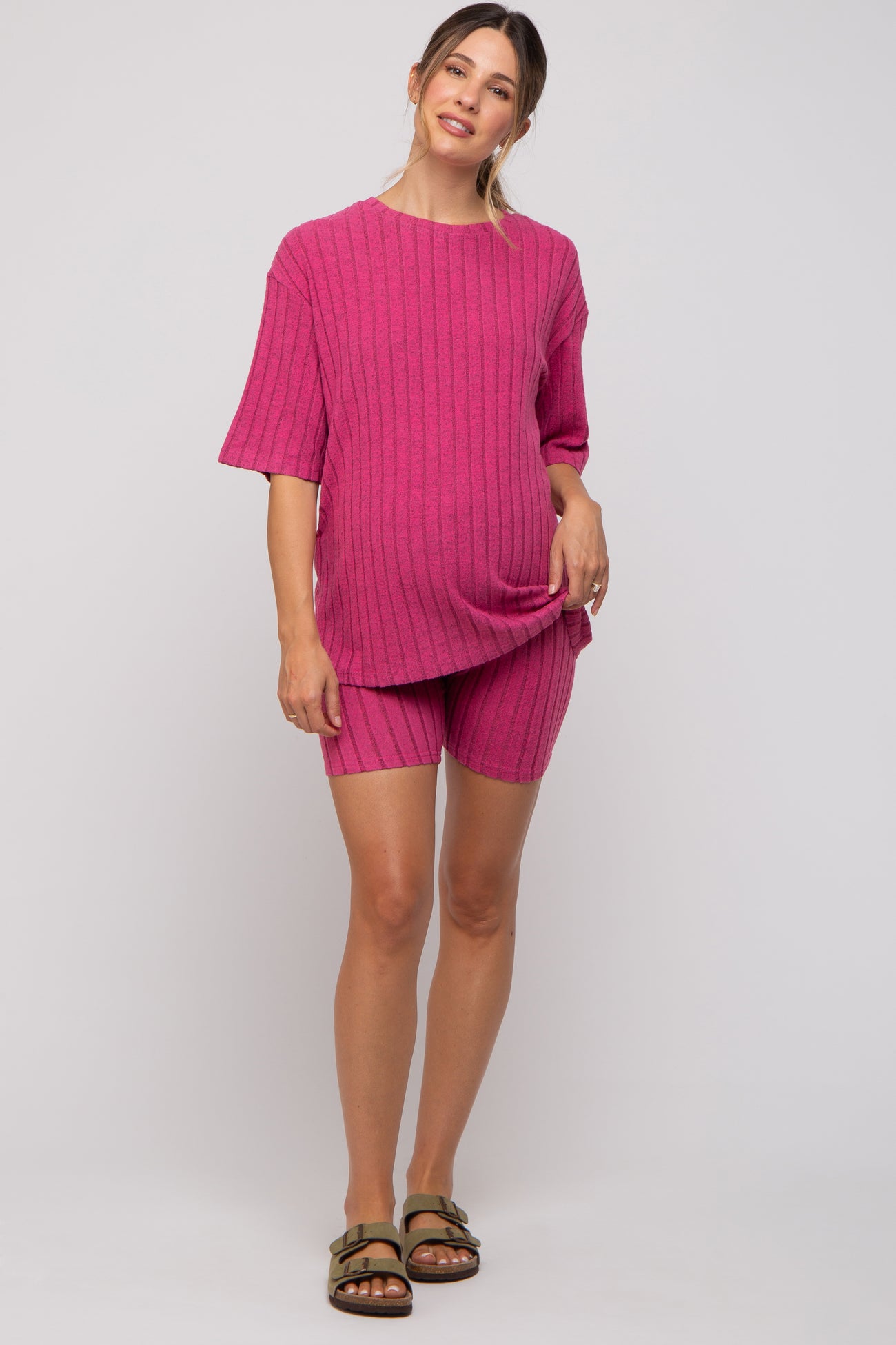 woman wearing a pink ribbed maternity set consisting of a short sleeve top and matching shorts, showing her baby bump