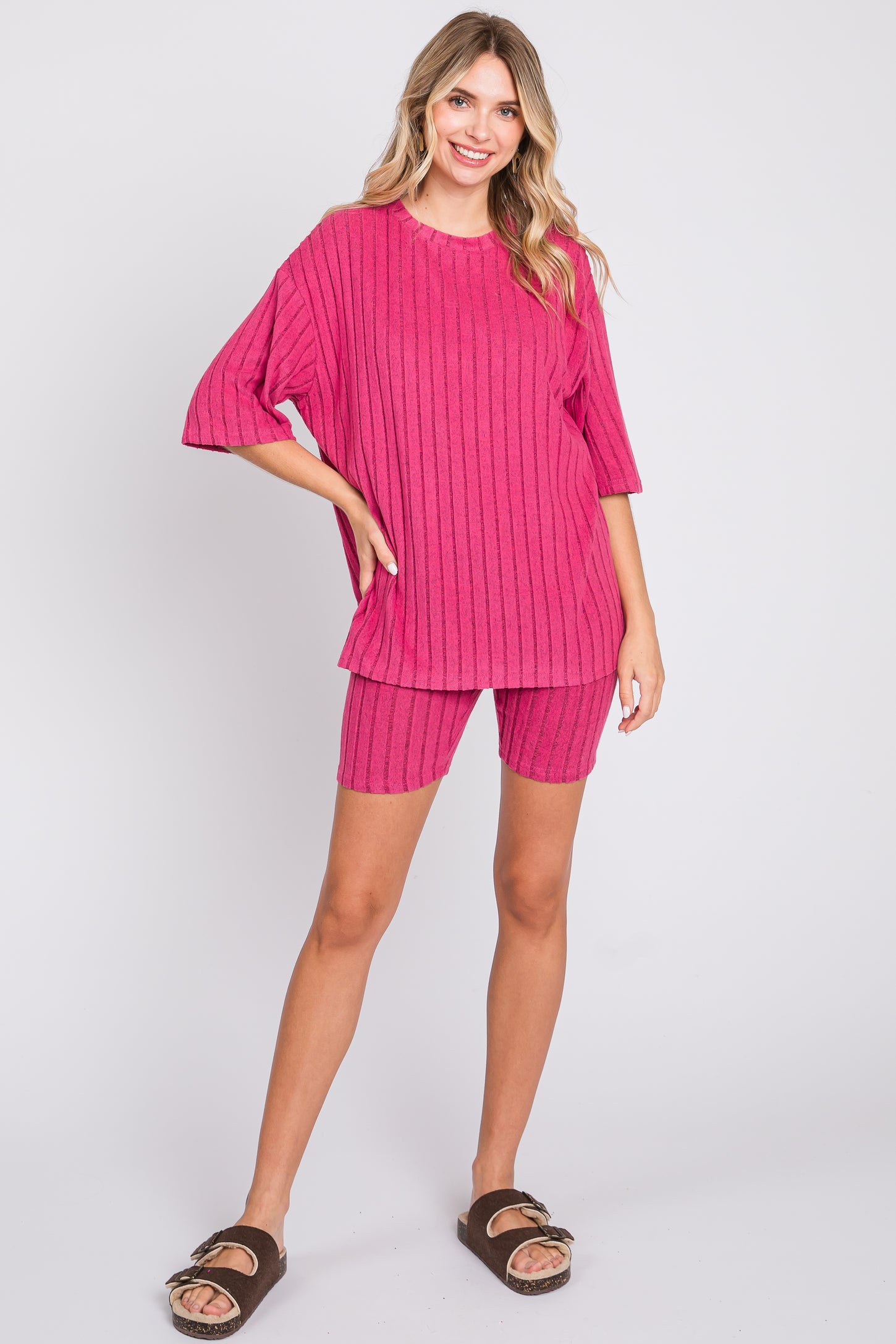 woman wearing a fuchsia pink oversized ribbed top with matching ribbed bike shorts and brown sandals