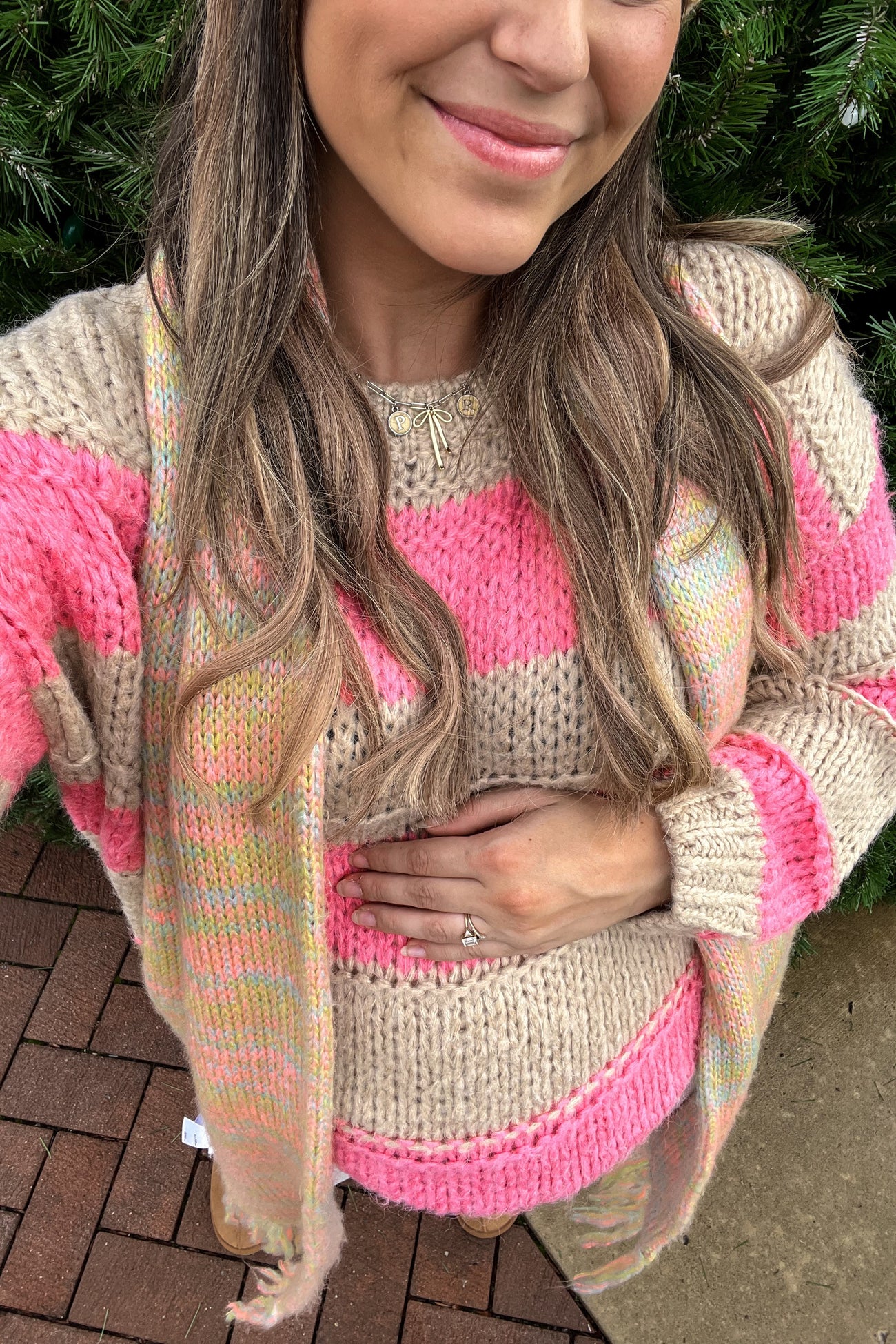 woman wearing a pink and beige striped maternity sweater and cardigan, gently cradling her baby bump