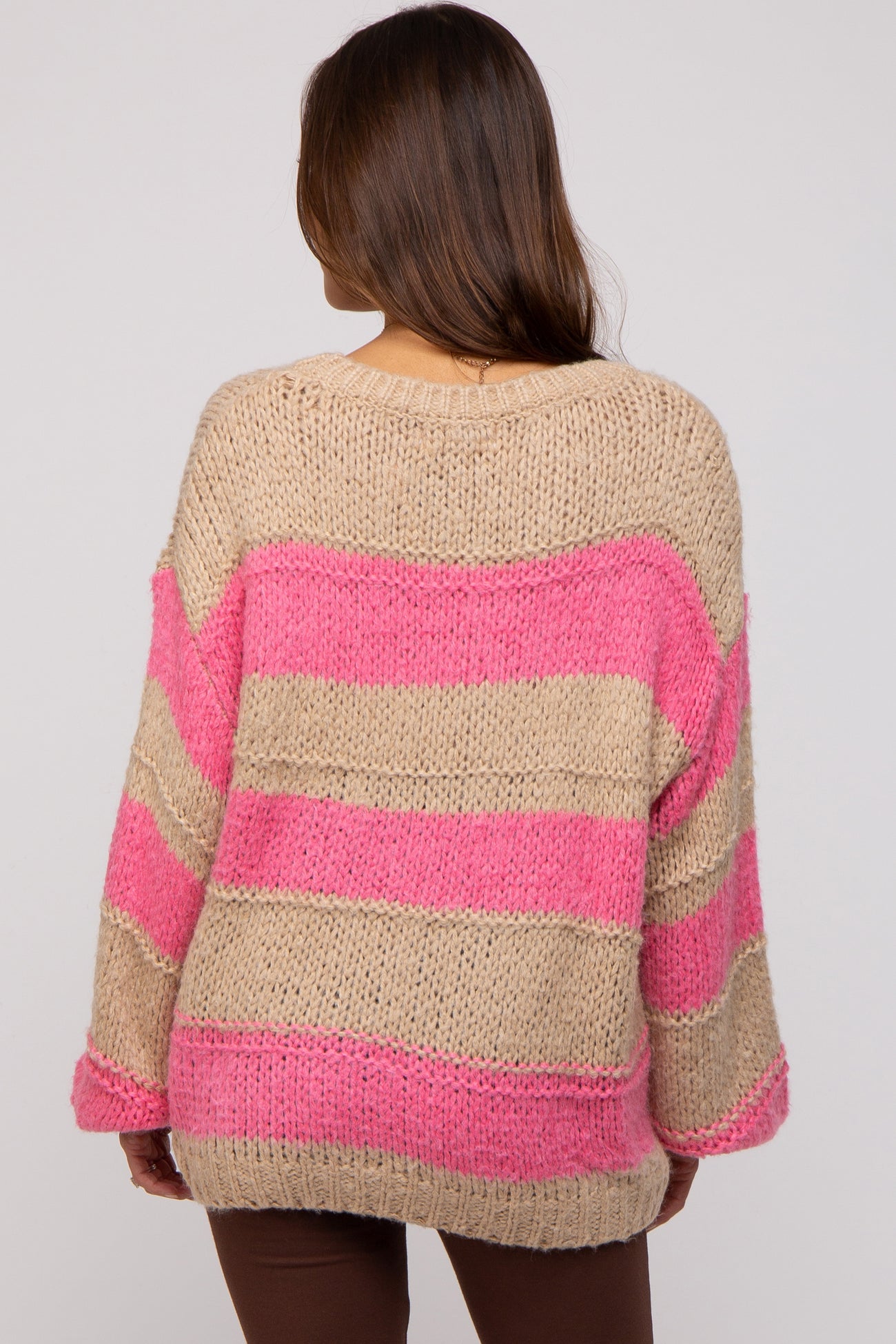 woman wearing a beige and pink striped oversized maternity sweater, showing the back view
