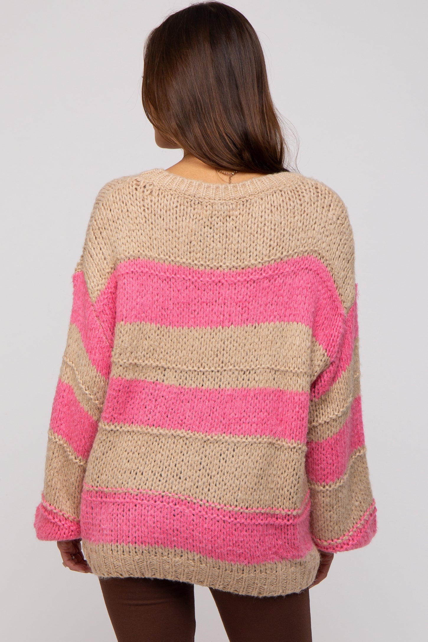 woman wearing a beige and pink striped oversized maternity sweater, showing the back view