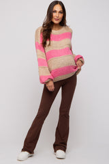 woman wearing a beige and pink striped maternity sweater with oversized sleeves and brown flared pants, showcasing her baby bump