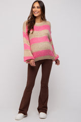woman wearing a beige and pink striped maternity sweater with oversized sleeves and brown flared maternity pants, showing baby bump